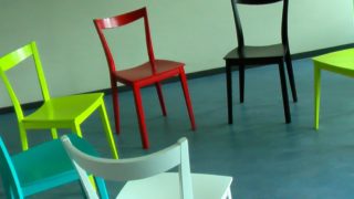 Vier bunte Stühle stehen im Halbkreis