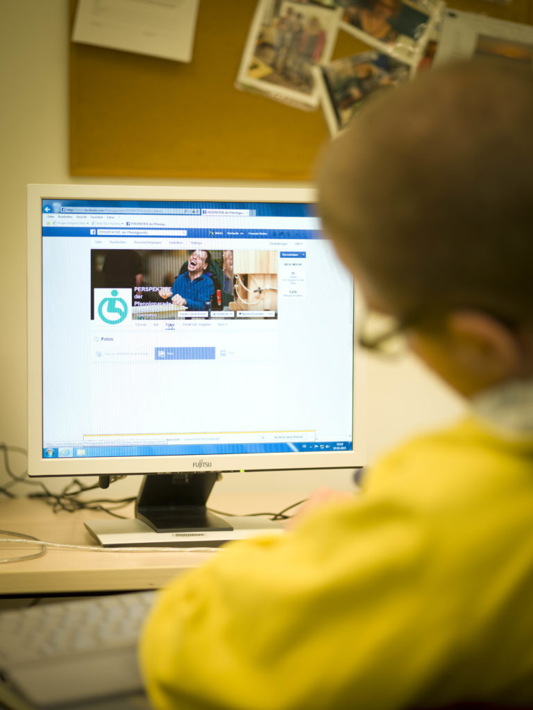 Ein Reha-Kunde sitzt vor dem Computerbildschirm und erstellt einen Facebookbeitrag