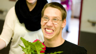 Ein Reha-Kunde hält eine Blume in der Hand und strahlt