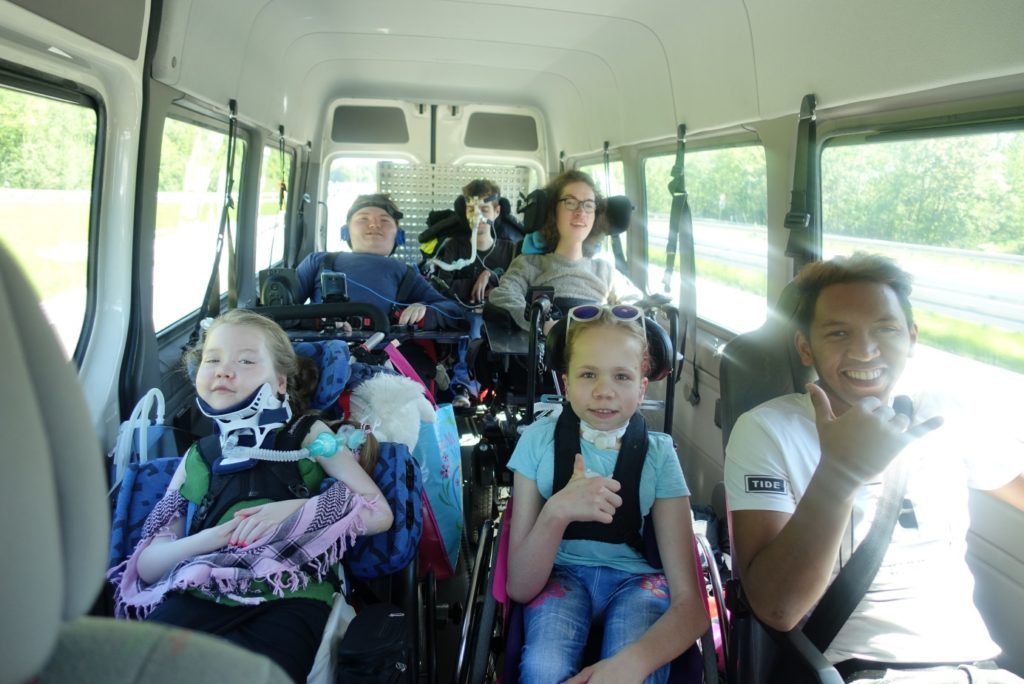 Einige Personen mit und ohne Rollstuhl und Atemgerät sitzen in einem Bus
