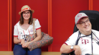 Zwei Personen im Bayern-Outfit in der Kabine des FC Bayern