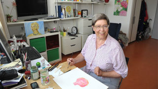 Eine AWG-Bewohnerin sitzt an ihrem Schreibtisch und malt ein Bild