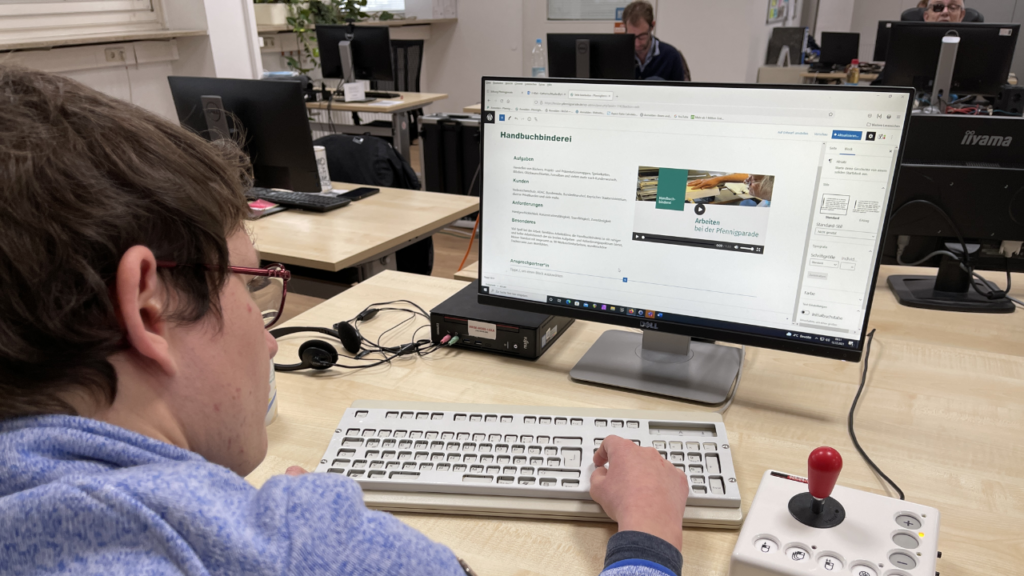 Werkstattmitarbeiter*in bei der Webseitenpflege mit Spezialtastatur und Joystick-Mouse