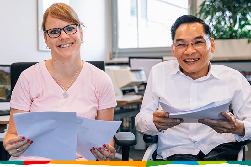 Zwei Mitarbeiter*innen halten Unterlagen in ihren Händen