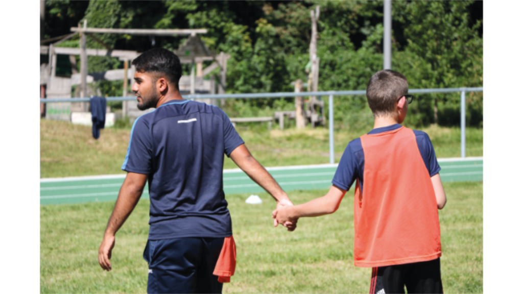 Zwei Personen schauen auf den Sportplatz und halten sich an den Händen