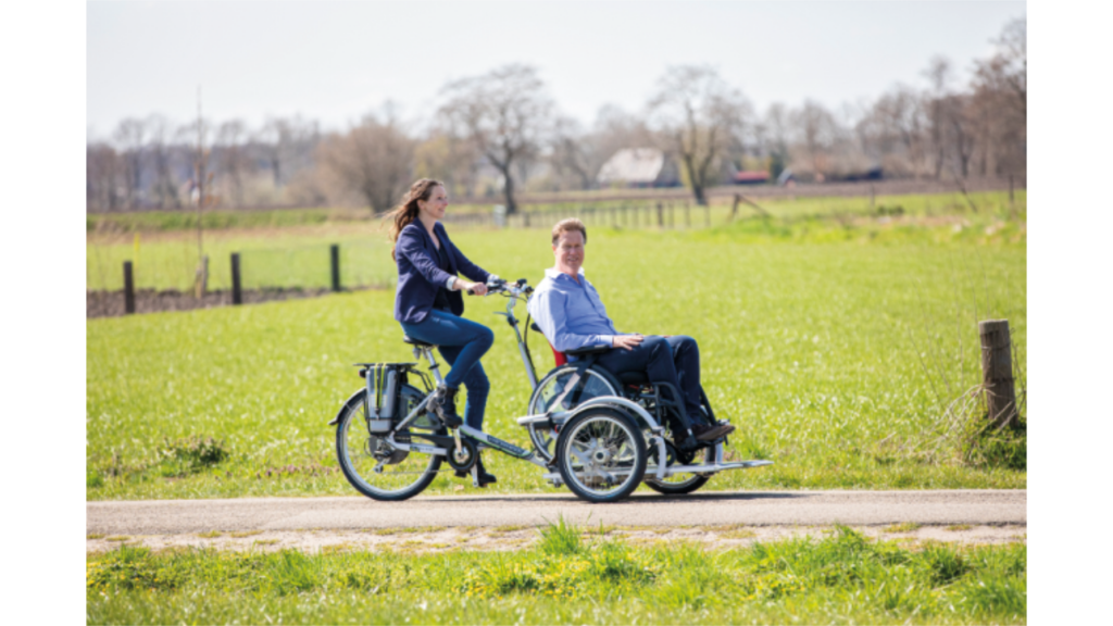 Zwei Personen mit einem Fahrrad mit Rollstuhlanhänger auf einem Feldweg