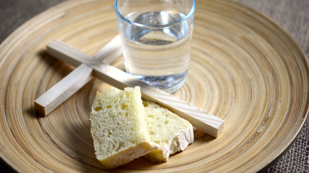 Teller mit einem Glas Wasser, ein Holzkreuz und Brot 