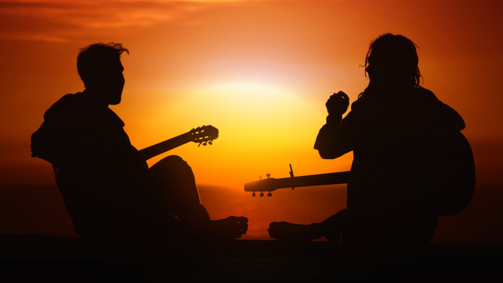 Zwei Personen mit Gitarren am Meer beim Sonnenuntergang