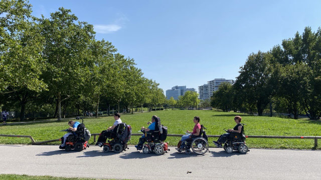 Mehrere Rollstuhlfahrer*innen hintereinander im Park