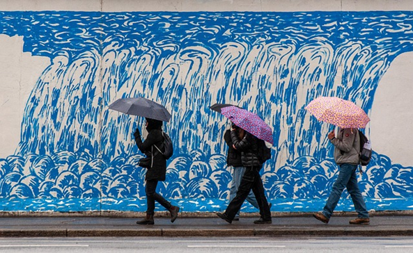 Vier Personen mit Regenschirm auf dem Gehweg.