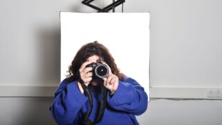 Frau im Rollstuhl fotografiert vor Leinwand mit Kamera