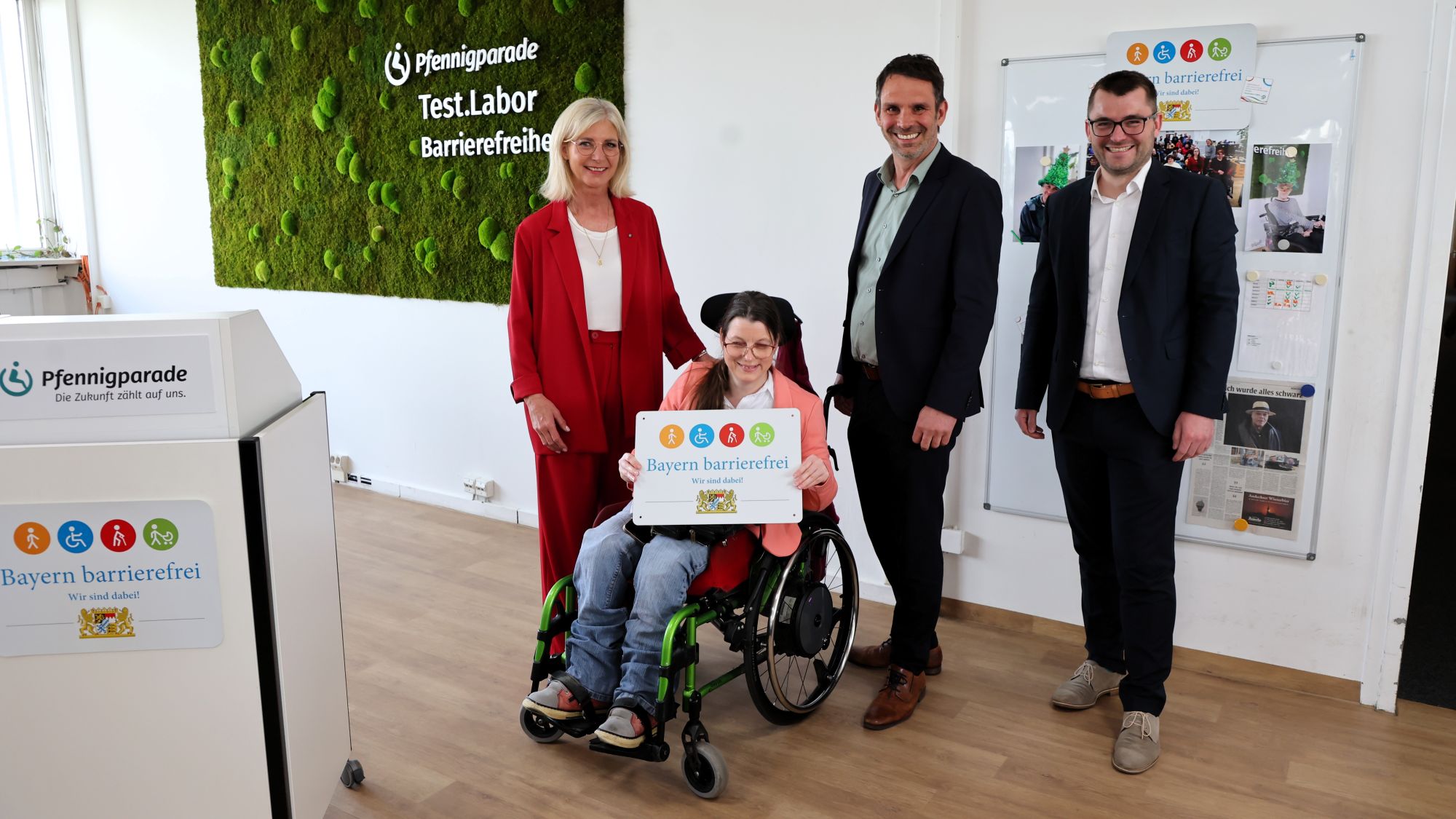 Mehrere Personen nebeneinander im Testlabor Barrierefreiheit mit Signe Bayern Barrierefrei. Eine davon im Rollstuhl
