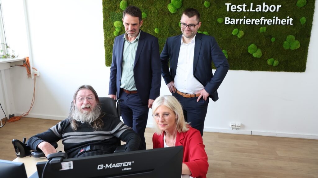 Vier Personen an Computerarbeitsplatz Text: Testlabor Barrierefreiheit