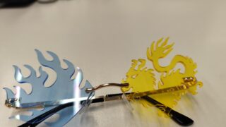 Gelbes Brillenglas in   Drachenform; Ein Blaues in Fischform und goldfarbenes Gestell